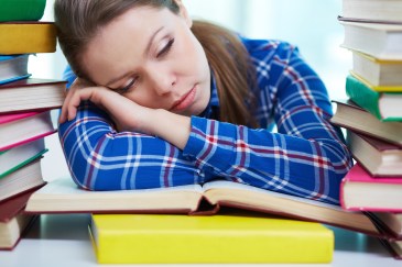 Tired student sleeping over textbooks